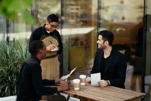 Waiter taking an order from two men in black sitting in a restaurant