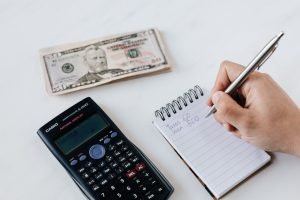 A calculator, dollar bills, and a notepad on a white surface