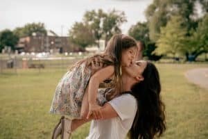 Mom lifting her daughter up and kissing her.