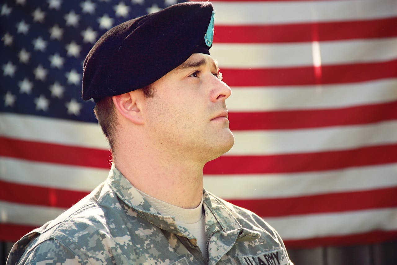 Man in camouflage in front of a U.S. flag.